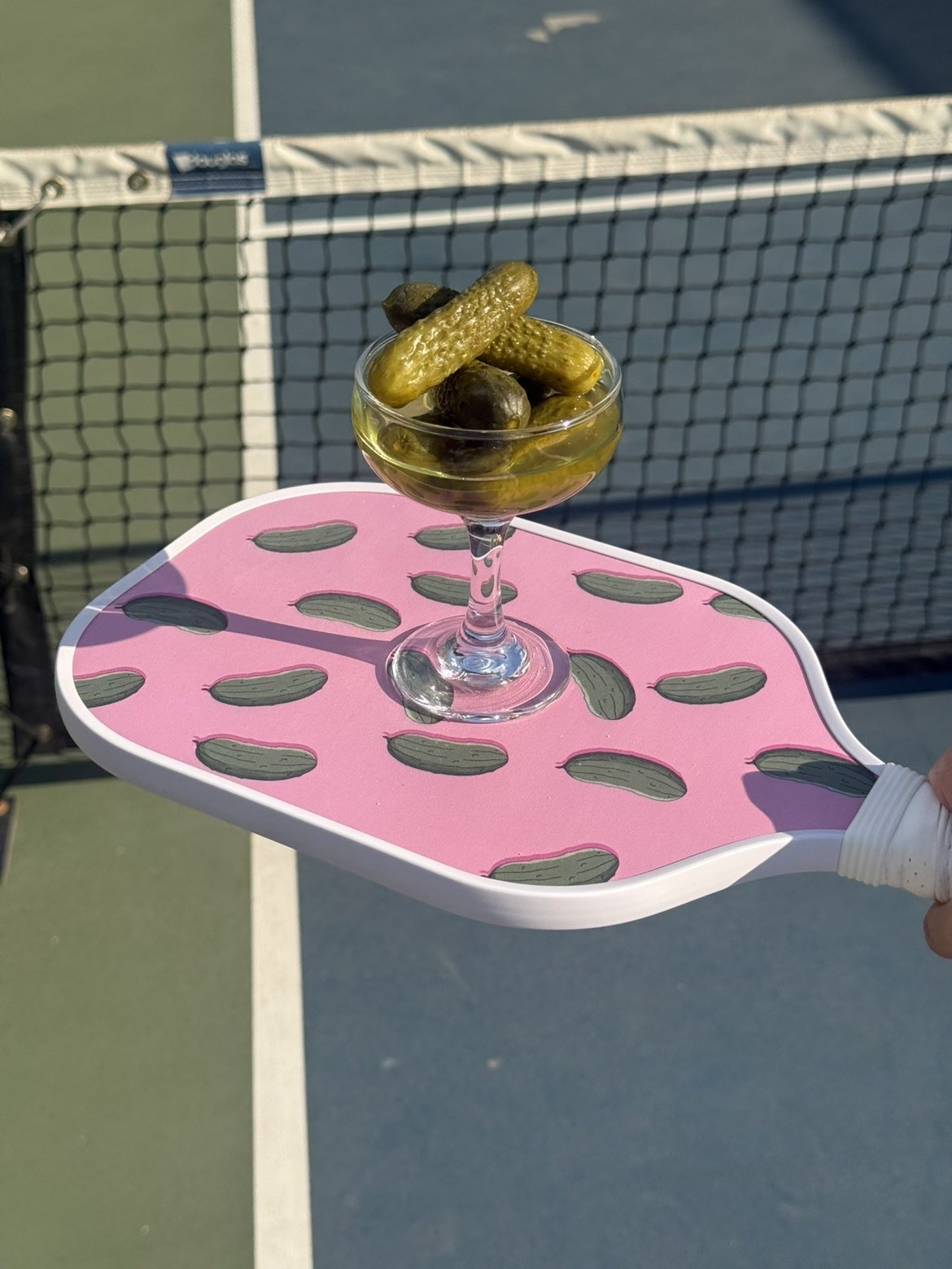 A coupe glass of pickles balanced on The Pink Paddle at the net